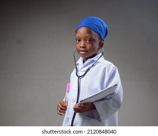 Cute African Career Girl Child Or Student In Laboratory Gown And With A Stethoscope, Acting Like Medical Practitioners Such As Doctor, Nurse Or Caregivers To Show The Benefit Of Science