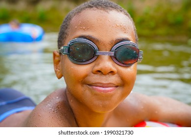 Cute African child boy close up portrait playing and relaxing in a buoy in a wild river and wearing glasses during summer holidays - Shutterstock ID 1990321730