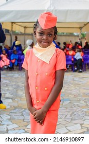 A Cute African Girl Child In An Orange Colored Air Hostess Outfit, Standing Outdoor In A School Gathering As They Celebrate Career Day