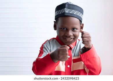 Cute African Muslim boy in traditional cloth plays and pretends to be a boxer, smiling and looking at the camera on white background - Powered by Shutterstock