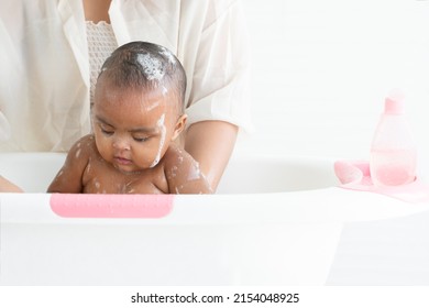 Cute African Newborn Baby Bathing In Bathtub With Soap Bubbles On Head And Body. Mother Washing Her Little Daughter In Warm Water. Newborn Baby Cleanliness Care Concept