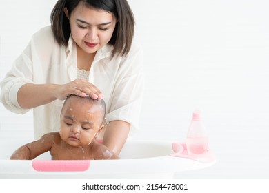 Cute African Newborn Baby Bathing In Bathtub With Soap Bubbles On Head And Body. Asian Young Mother Washing Her Little Daughter In Warm Water. Newborn Baby Cleanliness Care Concept