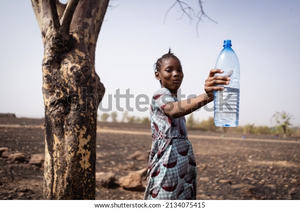Cute\
African village girl with a big mouthful of water in her mouth and\
holding aloft a plastic bottle, recommending the use of clean and\
fresh drinking water; disease prevention\
concept