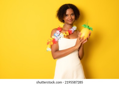 Cute African Woman Holding Pineapple Juice Wearing Flower Lei Necklace Standing Isolated Over Yellow Background.