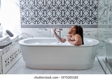 Cute African Woman Taking Bath With Bubbles In Bathroom Interior, Singing In Shower Handle, Have Fun. Lifestyle Wellness Concept. Treating Yourself And Wellbeing.