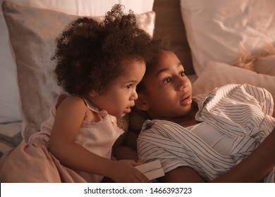 Cute African-American sisters watching cartoons in bedroom