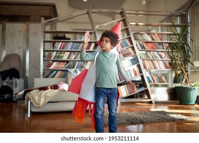Cute afro american kid playing with paper rocket at home