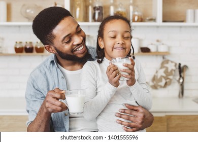 Cute afro child girl and her father drinking milk, having breakfast at kitchen. Happy family morning concept
