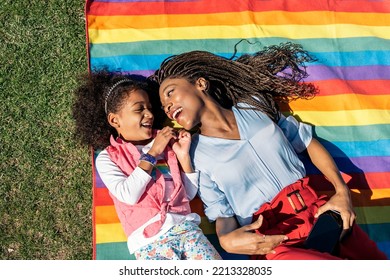 Cute afro girl lying down in the grass in colorful picnic blanket with her mom and enjoying sunny day. - Powered by Shutterstock