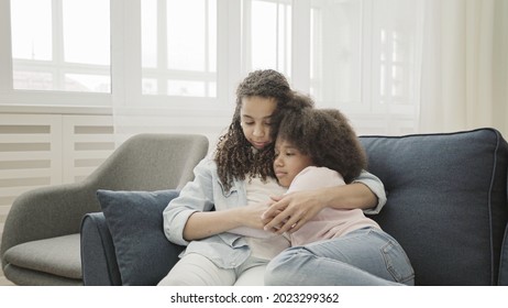Cute afro-american sisters sitting embraced on couch, family love and support