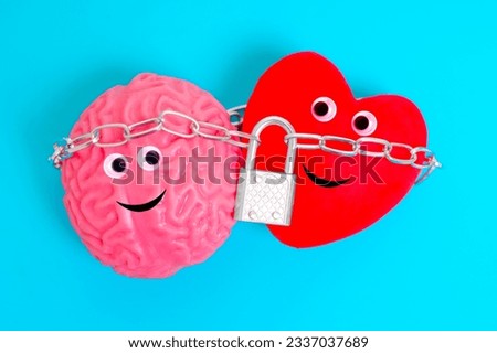 Cute anthropomorphic heart and brain characters, bound tightly together by a chain and secured with a padlock isolated on blue background. Intellect and feelings related concept.