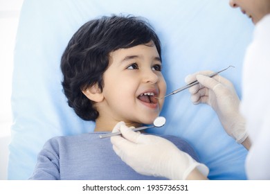 Cute arab boy sitting at dental chair with open mouth during oral checking up with doctor. Visiting dentist office. Stomatology concept - Powered by Shutterstock