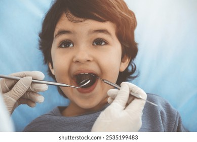 Cute arab boy sitting at dental chair with open mouth during oral checking up with doctor. Visiting sunny dentist office - Powered by Shutterstock