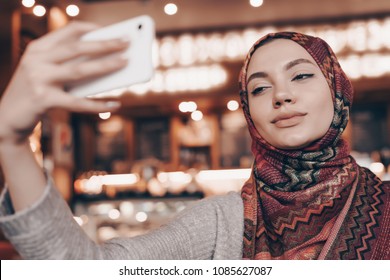 Cute Arab Girl In Beautiful Headscarf Doing Selfie, Sitting In Cafe And Smile 