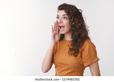 Cute armenian curly-haired girl yelling loud turn left hold palm open mouth calling brother come down dinner ready standing white background shouting searching friend crowded party