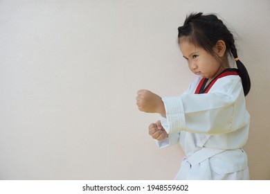 A cute Asia girl standing in taekwondo suit with white wall on background for waiting to study on the activity at the school.Learning and exercising from activities on the holiday.