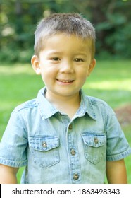 A Cute Asian American Boy Wearing A Jean Fabric Button Up Shirt. He Is Outside. Smiling Straight On. 