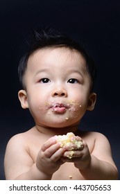 Cute asian baby boy eating cake with his both hand and messy on his face