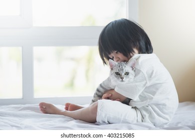 Cute asian baby playing with American Shorthair kitten on white bed
