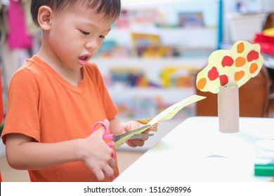 Cute Asian Boy Cutting A Piece Of Paper, Introduce Scissor Skills For Toddlers, Little Kid Enjoying Doing Arts & Crafts, Children's Art Project, DIY Toys For Kids From Recyclable Materials Concept