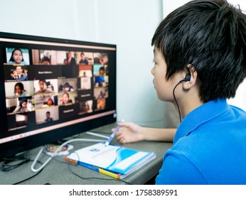 Cute Asian Boy With Earphone, Sitting At Desk ,using Pc For Having Video Conference Chat With Teacher And Class Group At Home. Study Online Remote Learning, Homeschooling During Coronavirus Outbreak.