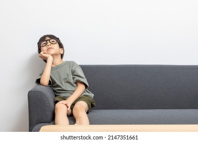 Cute Asian Boy With Eyeglasses Looking Up Or Right, Sitting On A Sofa At Home.