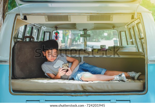 A cute\
Asian boy in a family van, lie about on a relaxing car by watching\
a smartphone, on a weekend\
vacation.