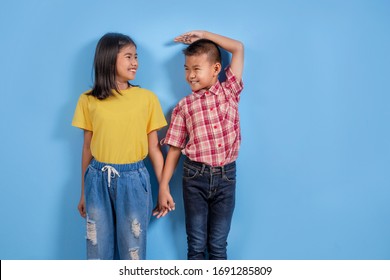 Cute Asian Boy And Girl Measuring Their Height On Sky Blue Background