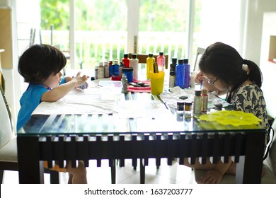 Cute Asian Boy And Girl Painting Rocks On Table. Summer Activity For Children.Stone Art For Kids.Colorful Paint Bottles.Huge Door With Bright Sun At Background.Homesetting Activity For Homeschoolers.