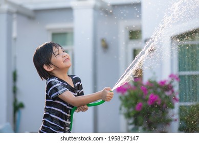 Cute Asian Boy Has Fun Playing In Water From A Hose Outdoors