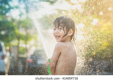 Cute Asian Boy Has Fun Playing In Water From A Hose Outdoors