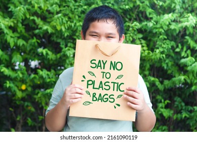 süßer asiatischer Junge, der braune Papiertüte auf grünem Hintergrund hält. Sag nein zu Plastiktüten. Umweltfreundliches Konzept.