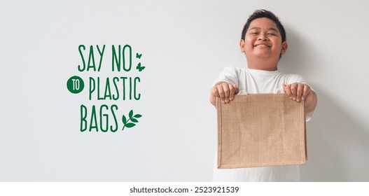 Cute Asian boy holding jute bag or sack bag on gray background. Reusable shopping bag. Natural material. Zero waste. Plastic free. Eco friendly concept. - Powered by Shutterstock