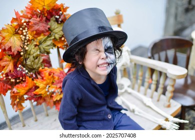 Cute Asian Boy Wearing Halloween Costume.Child With Skeleton Facepaint.Kid With Black Hat Sitting In Outdoor.Preschooler Trick Or Treating In Outdoors.Beautiful Decoration Setting In October.