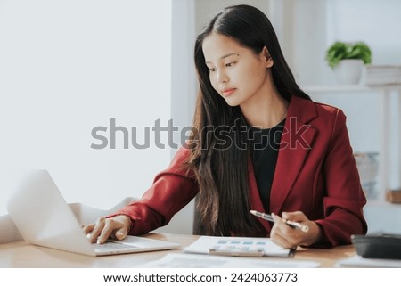 Cute Asian businesswoman in suit in modern workplace. Thai woman. Southeast Asian woman. looking at laptop in office
