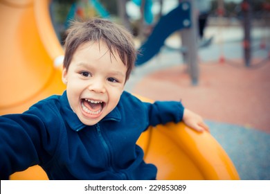 Cute Asian Caucasian Mixed Race Toddler Happily Playing On A Slide In A Playground Outside In The Summer Sun