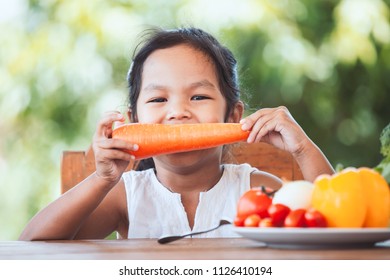 Cute Asian Child Girl Eating Carrot And Learning About Vegetables With Happiness