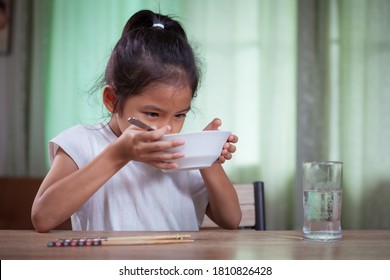 Cute asian child girl eating delicious instant noodles and drinking soup from bowl for her lunch in the house - Powered by Shutterstock