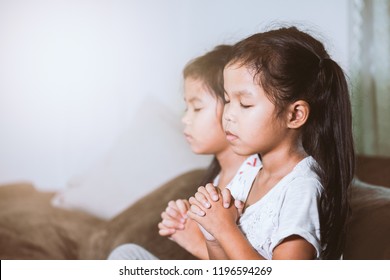 Cute asian child girl and her sister praying with folded her hand in the room together for faith,spirituality and religion concept