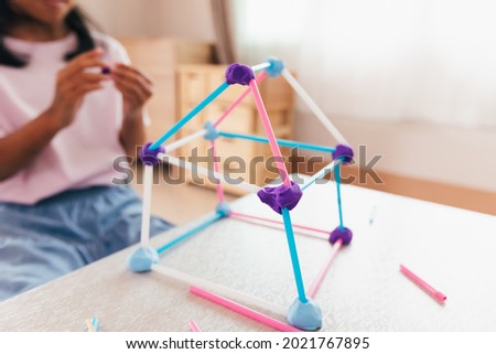 Cute asian child girl playing and creating with playdough and straws. Child concentrated with playdough building a molecule model. Kid and craft with recycle things.