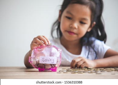 Cute Asian Child Girl Putting Money Into Piggy Bank To Save Money For The Future