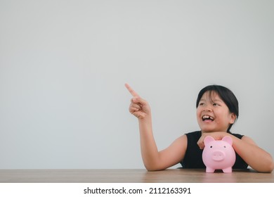 Cute Asian Child Girl Putting Money Into Piggy Bank To Save Money For The Future