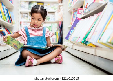 Cute Asian Child Girl Select Book And Reading A Book In Bookstore In Supermarket