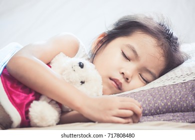 Cute Asian Child Girl Sleeping And Hugging Her Teddy Bear In The Bed