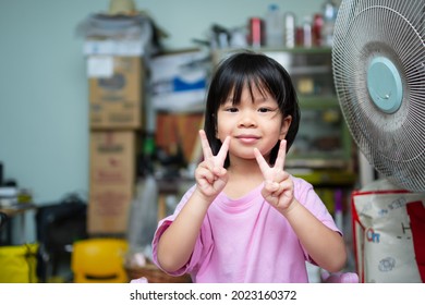 Cute Asian Child Girl Sweet Smile. Happy Kid Raise Finger In A V Shape, Raise Her Index And Middle Fingers. Children In A Good Mood.