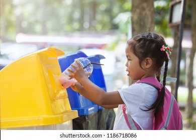 Cute Asian Child Girl Throwing Plastic Glass In Recycling Trash Bin At Public Park