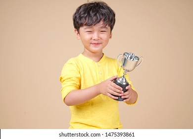 Cute Asian Child Holding Up A Winning Trophy, Isolated On Background