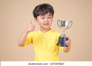 Cute Asian Child Holding Up A Winning Trophy, Isolated On Background