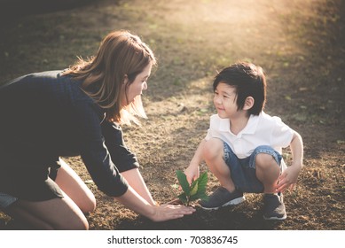 Cute Asian Child And Mother Planting Young Tree On The Black Soil