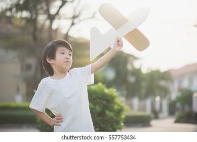 Cute Asian Child Playing Cardboard Airplane In Thee Park Outdoors